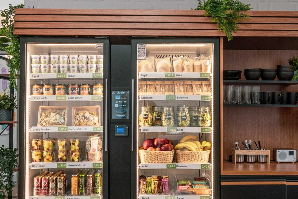 Smart Fridge mit frischen Bowls, Obstkörben und Getränken vor dunklem Holzregal mit Pflanzen